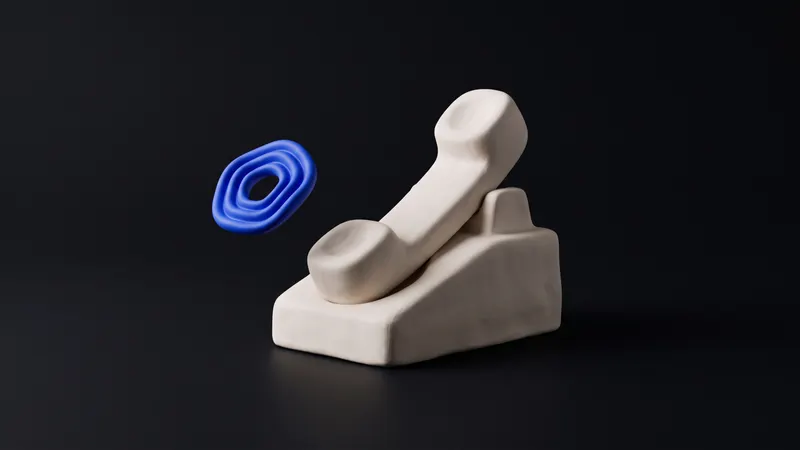 A matte clay telephone handset in off-white with a small cobalt dial accent, resting on a warm off-white background