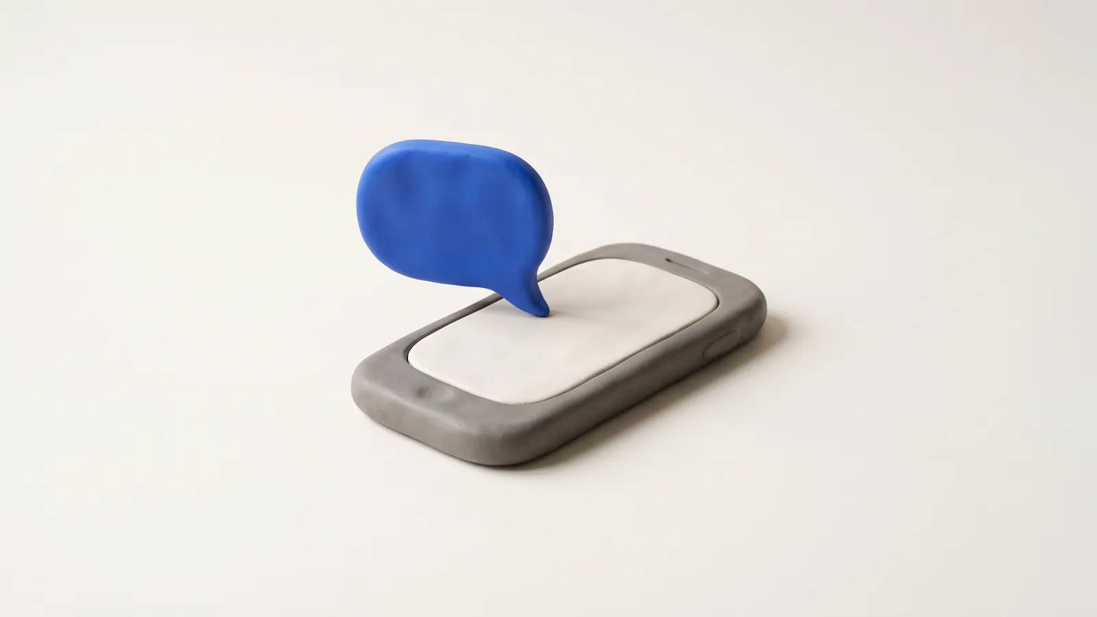 A matte clay phone with a small cobalt message bubble floating beside it, on a near-black background